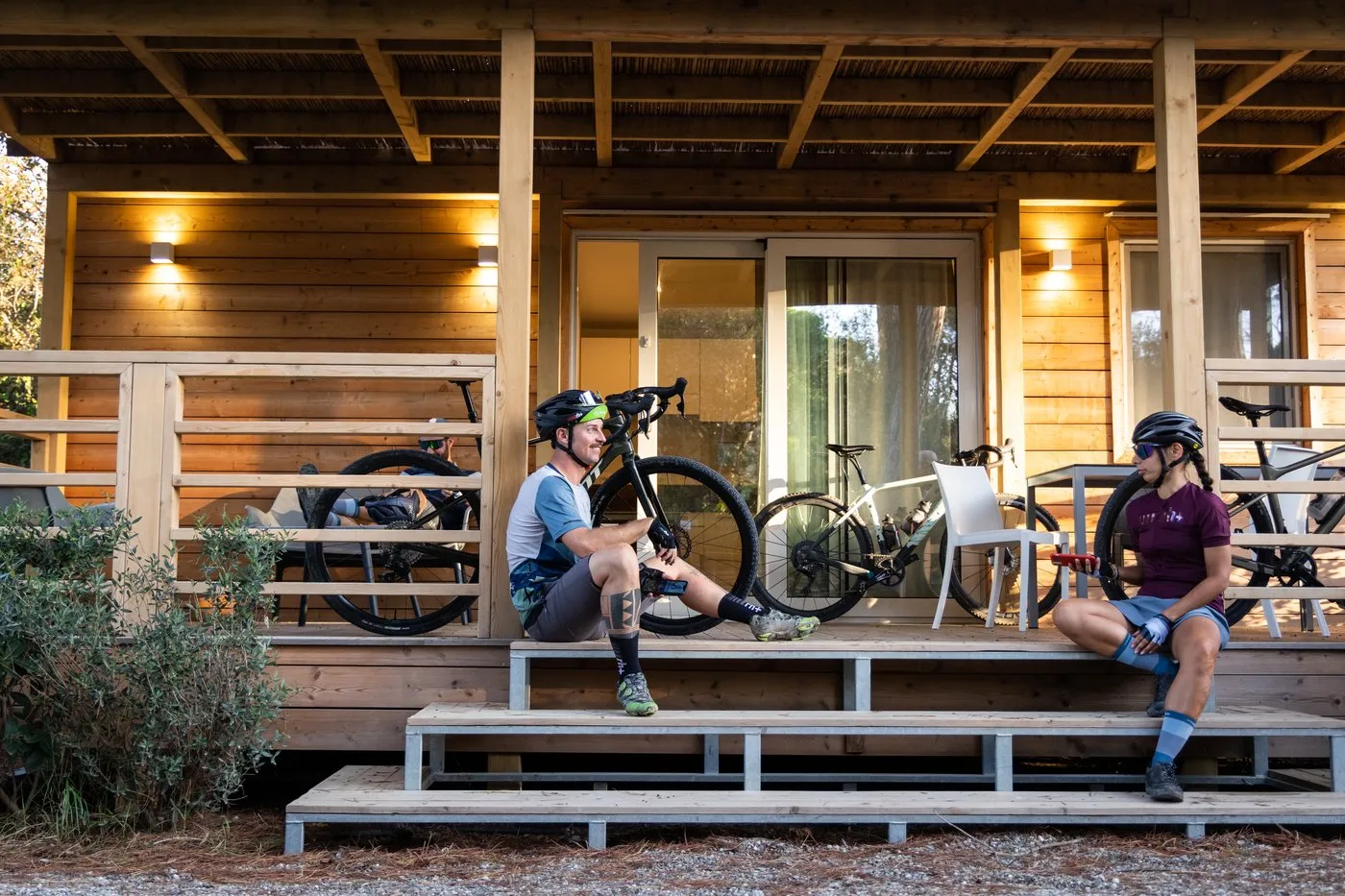 Cyclists with their gravel bikes on the porch of a wooden lodge at PuntAla Camp &amp; Resort
