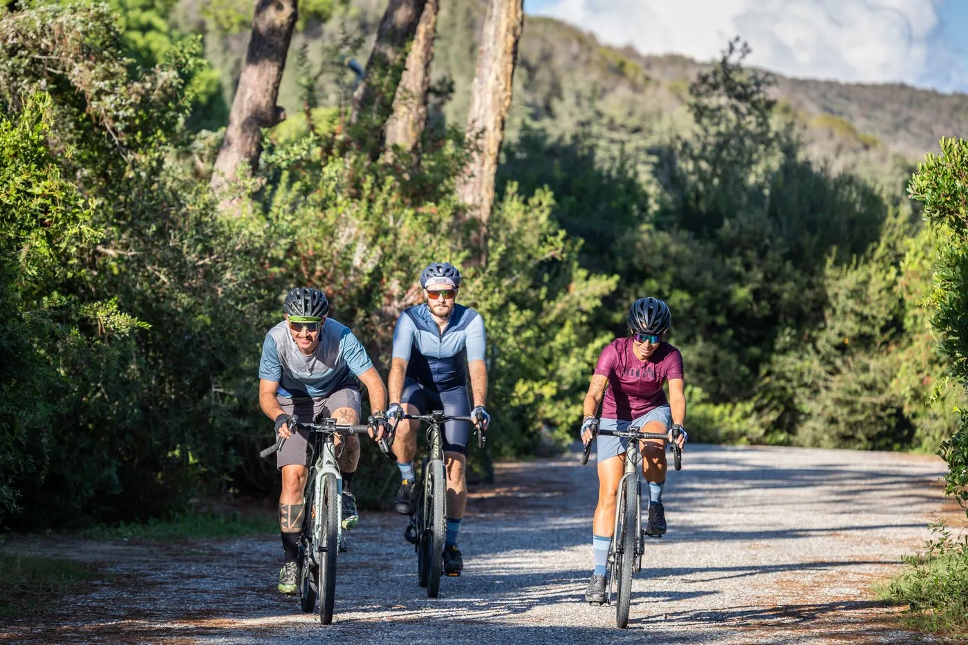 Three cyclists riding a white gravel road under the pines near Punta Ala